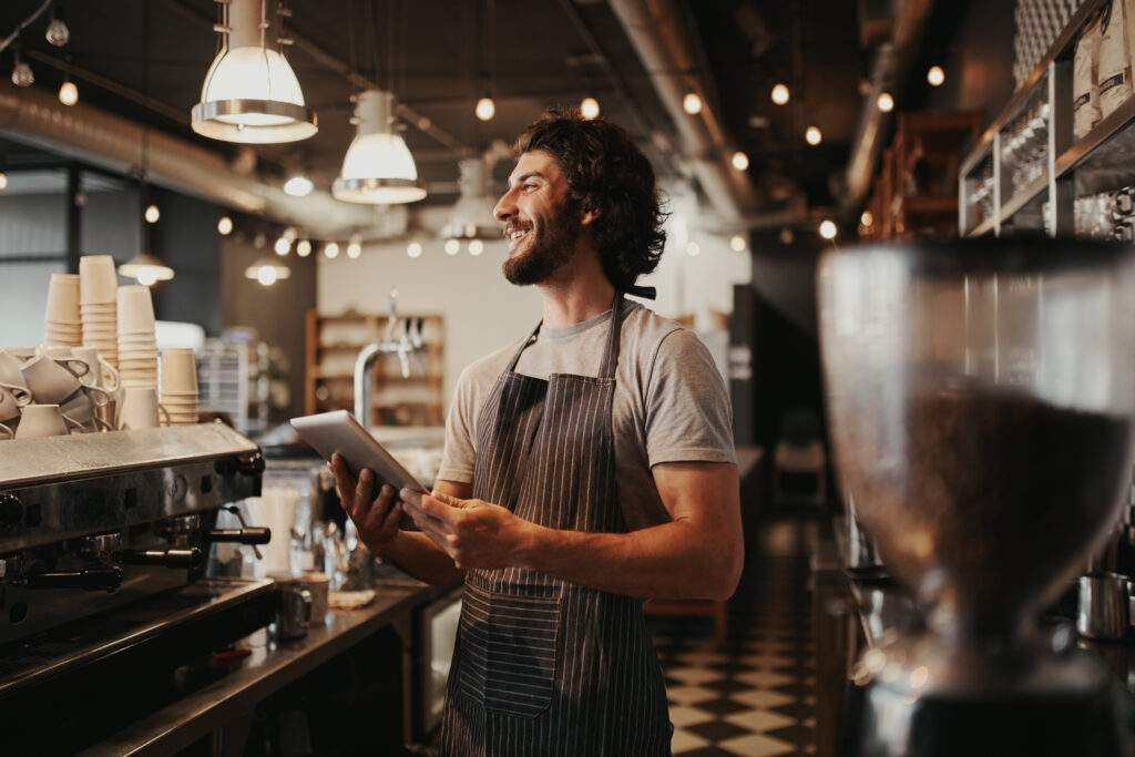 self-employed mortgages Handsome caucasian man in coffee shop laughing while holding digital tablet in hand standing behind counter