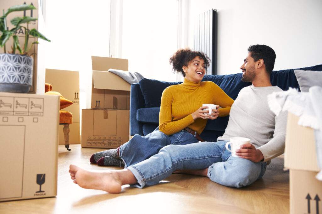 first time buyer Young Couple In New Home Drink Coffee Sitting On Floor In Lounge